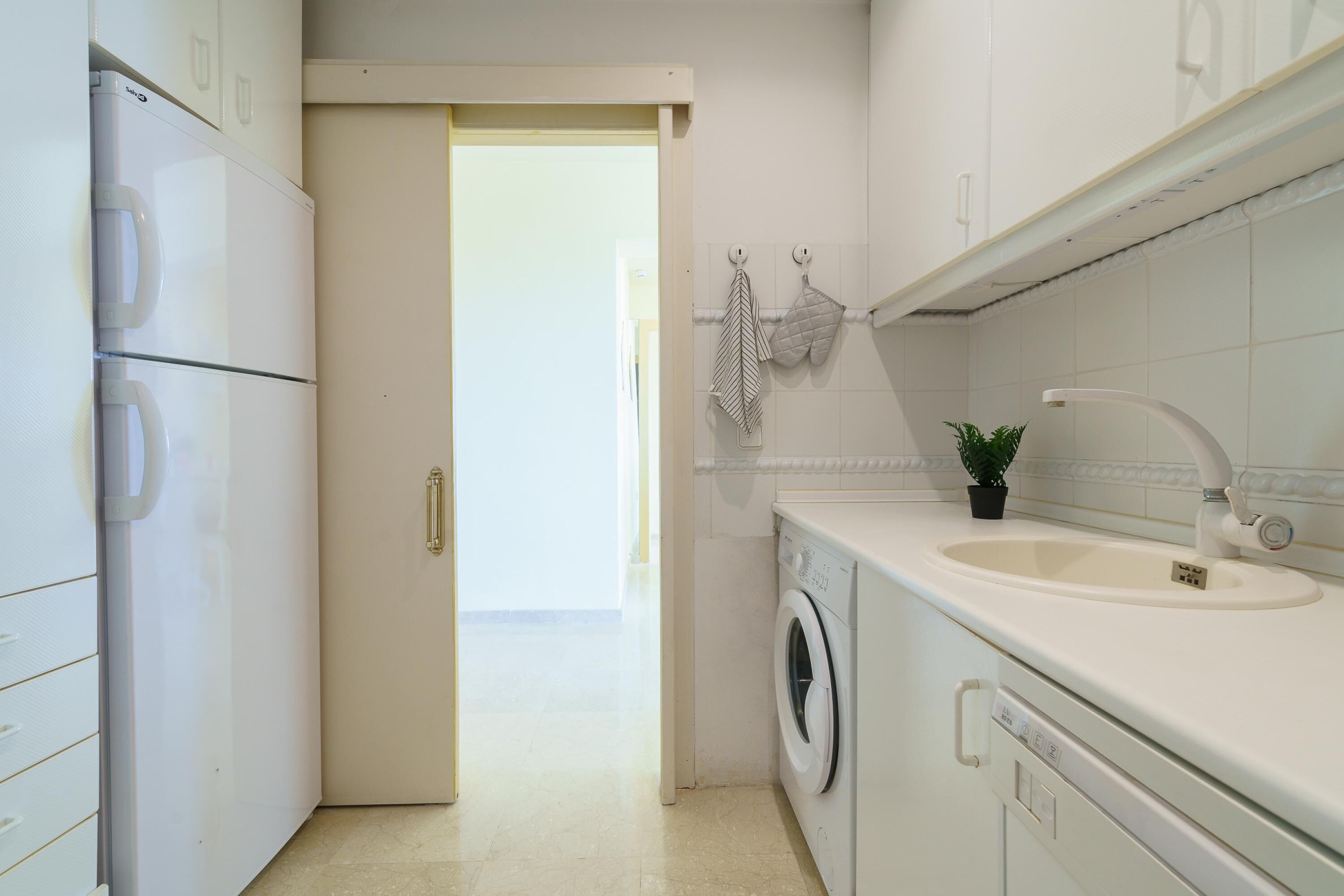 Una cocina con lavadora, un lavamanos y una puerta que da a otra habitación.