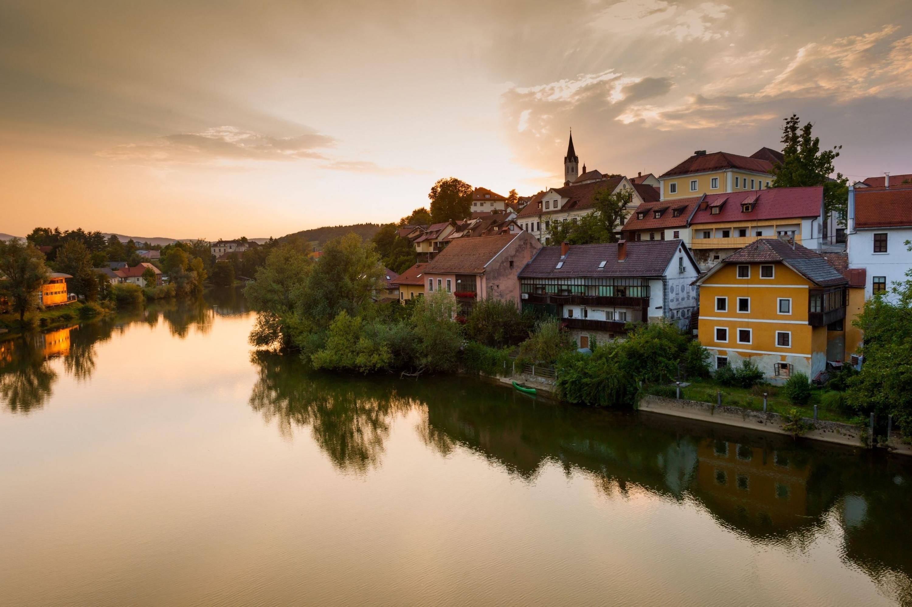 A riverside town with historic buildings, a church, and a calm water body reflecting the structures.