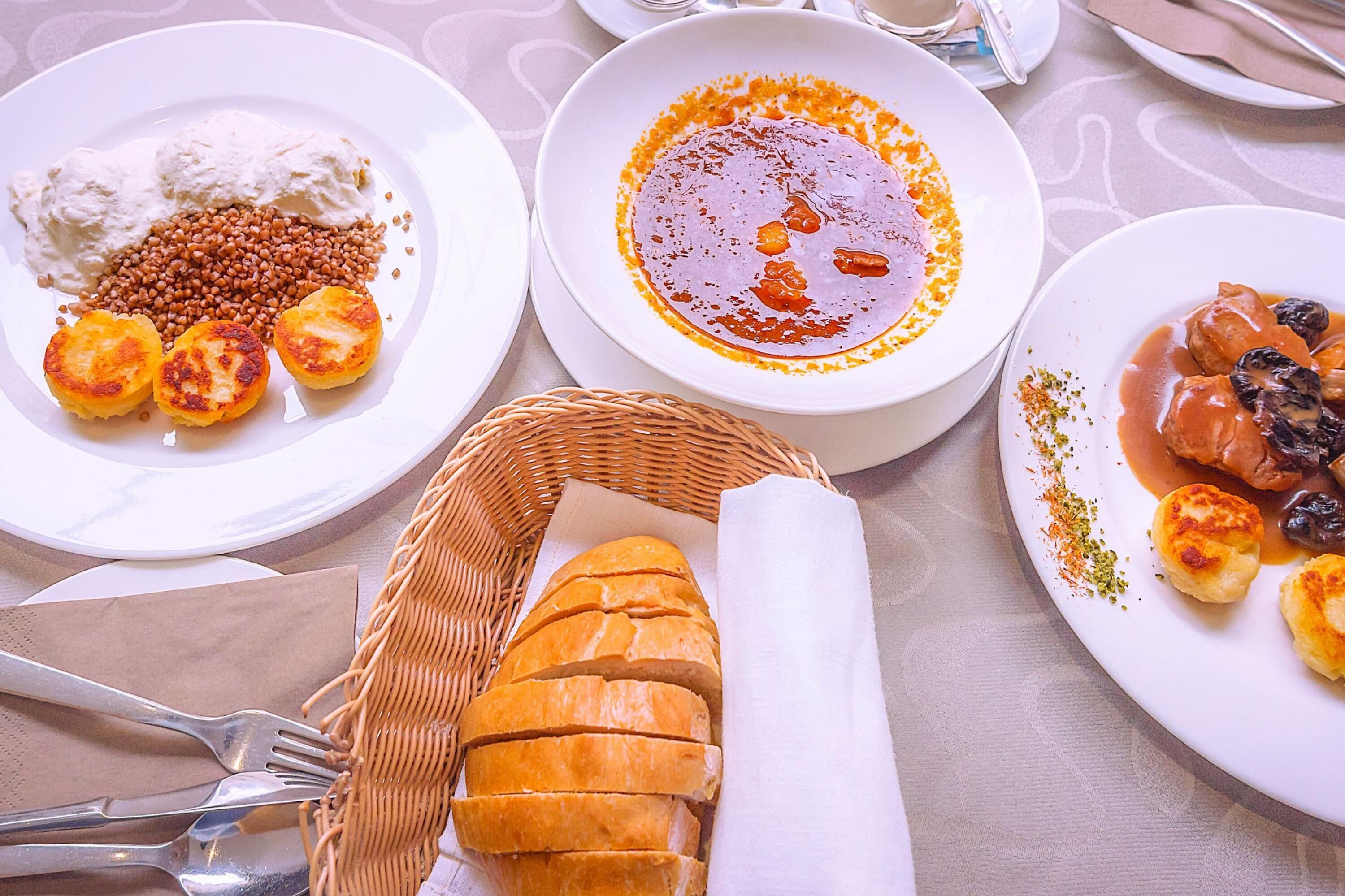A table with plates of food, a basket of sliced bread, and a fork.