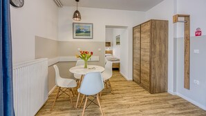 Een moderne kamer met een houten vloer, een ronde eettafel met witte stoelen, een klok aan de muur en een ingelijste foto boven de tafel.