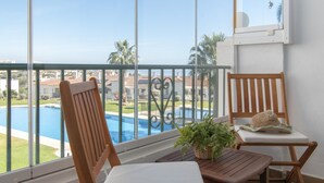 A balcony with a view of a swimming pool, two wooden chairs, a small table, and a potted plant. - Rancho Miraflores in Las Lagunas de Mijas (Mijas)