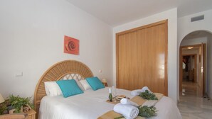 A neatly made bed with a headboard, a wooden wardrobe, and a wicker side table with a plant. - Rancho Miraflores in Las Lagunas de Mijas (Mijas)