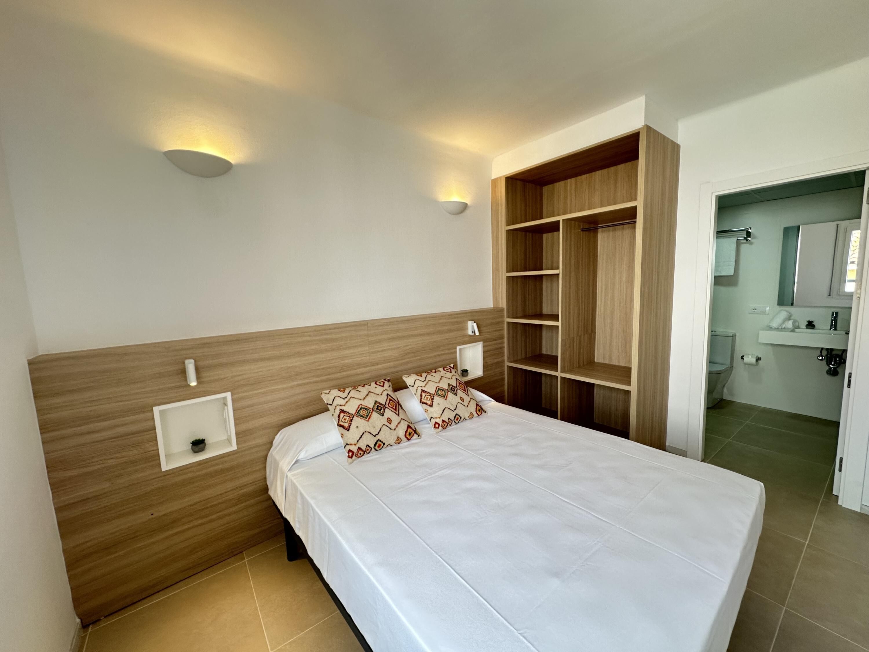 A neatly arranged bedroom with a bed, bedside tables, a built-in wardrobe, and a bathroom visible through an open door.
