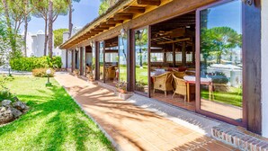 A covered outdoor seating area with glass walls, wicker furniture, and a tiled patio. - Marbella Resort 5 Pool Whirlpool Sauna (Marbella)