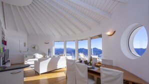 Quarto espaçoso com piso de madeira, móveis brancos, grandes janelas e vista para montanhas.