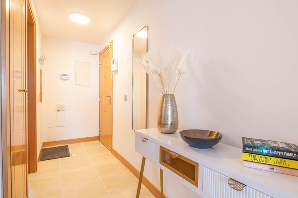 A hallway with a white console table, a mirror, a vase with dried flowers, and a few books. - Sunset Golf International (Estepona)