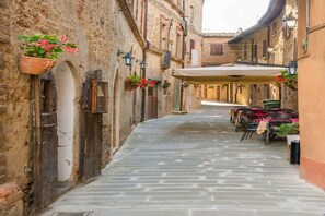 A narrow stone-paved alley with rustic buildings, outdoor seating, and hanging flower pots. - Olive Brench Apt In Farmhouse With Pool (Panicale)