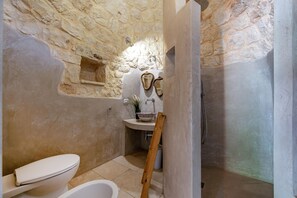 Een badkamer met een stenen muur, toilet, badkuip en wastafel met spiegel en plant.