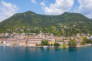 A coastal town with a prominent mountain in the background, a marina with boats, and a mix of residential and commercial buildings. - Perla del Lago Near the Beach (Salò)