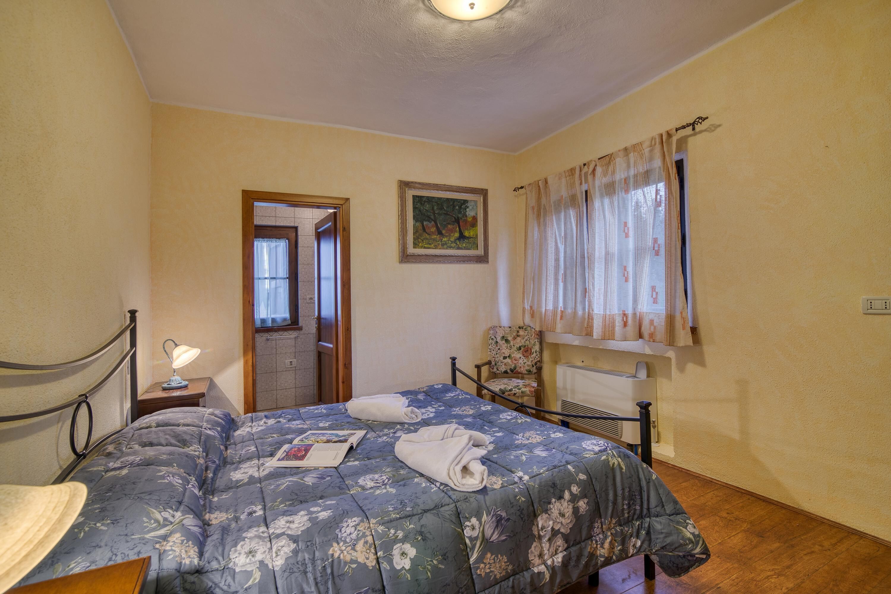 Une chambre à coucher avec un lit, une chaise, un tableau et une fenêtre avec des rideaux.