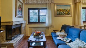 A living room with a fireplace, a sofa, a coffee table with a fruit arrangement, and a painting of sunflowers. - Tenuta Di Litiano With Pool (Roccastrada)