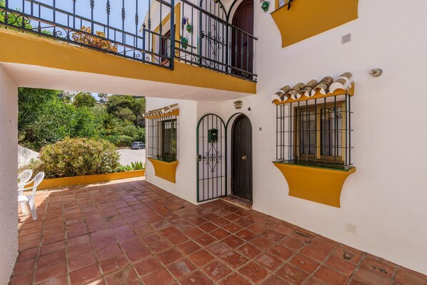 A courtyard with a tiled floor, a balcony with black railings, and a door with a decorative gate. - Sunny Tranquility With Pool (Benalmádena)