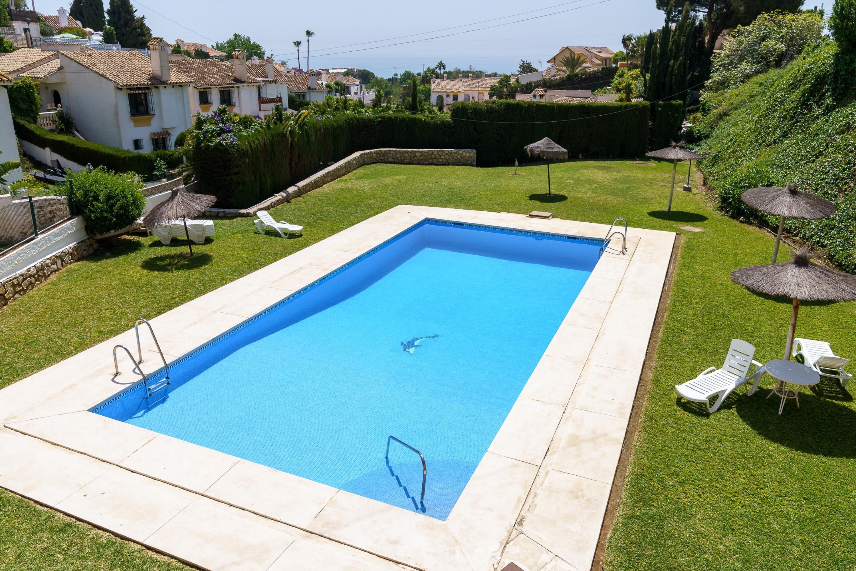 A rectangular swimming pool with a diving board and a ladder, surrounded by a well-maintained lawn and white lounge chairs.