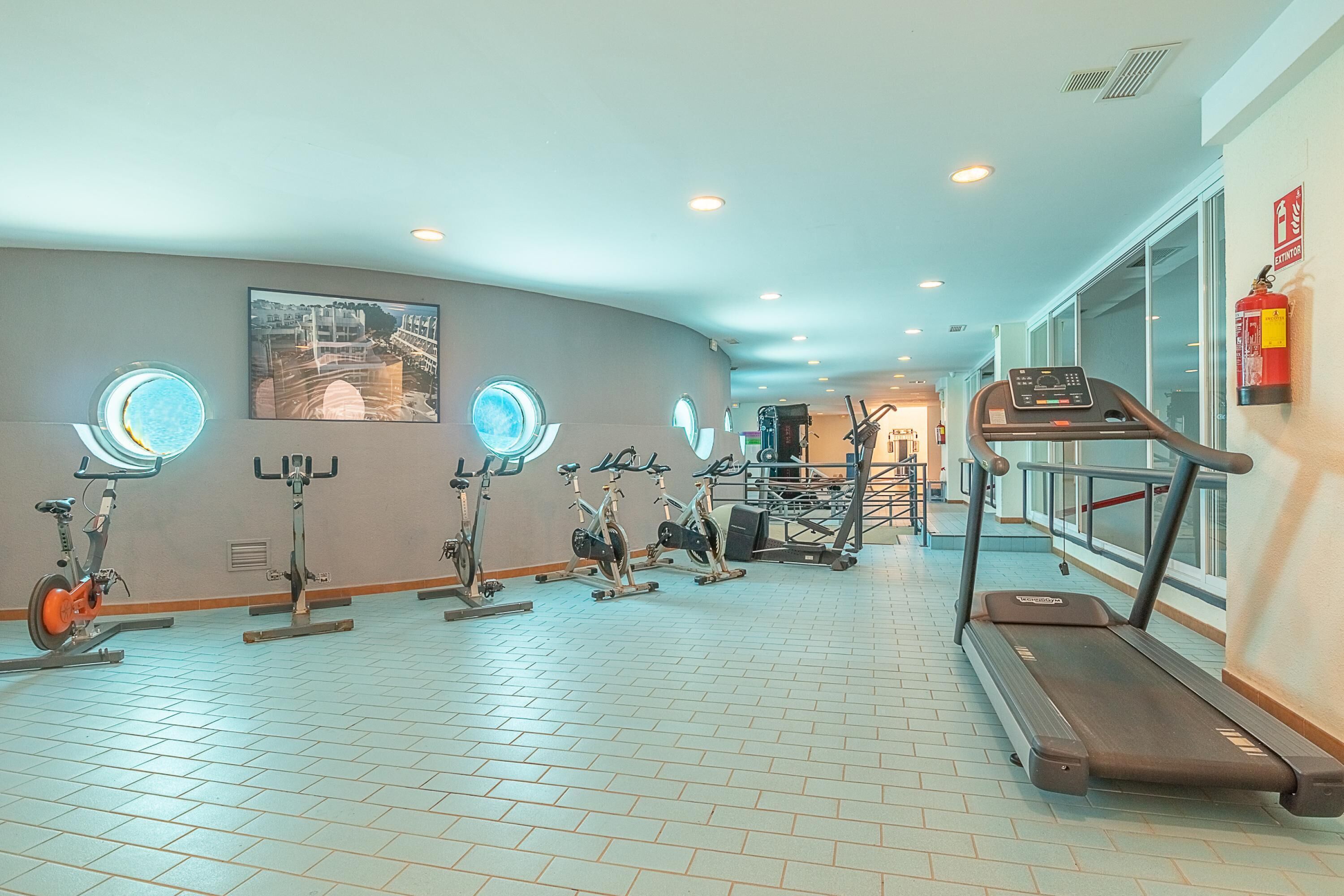 Et fitnesscenter med motionscykler, løbebånd og en fastmonteret brandslukker.