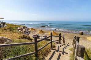 Una escalera de madera que conduce a una playa con sombrillas de paja y sillas reclinables.