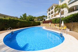En swimmingpool med kristallklart blått vatten, omgiven av en kakelbeklädd terrass och gula solstolar.