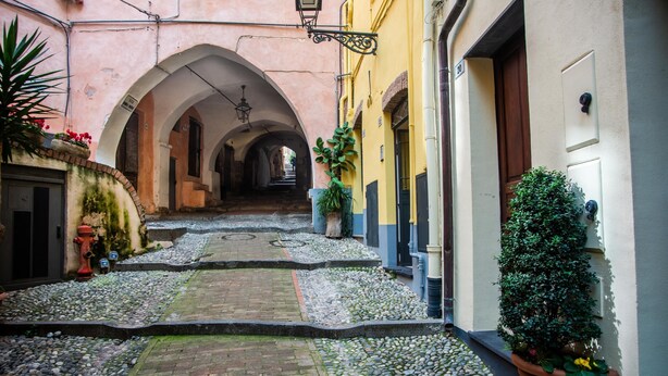A narrow alleyway with cobblestone pavement, arches, and potted plants. - Casa Felice in San Remo (Sanremo)