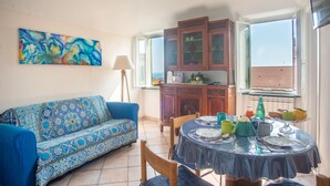 A dining area with a blue patterned sofa, a round table with blue tablecloth, and a cabinet with glass doors. - Casa Felice in San Remo (Sanremo)