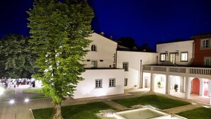 Un patio con un árbol grande, una fuente rectangular y un edificio con varias ventanas y un balcón.