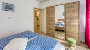 A bedroom with two beds, a wooden wardrobe, a green stool, and a framed picture on the wall. - Apartments Jantar - Two Bedroom n 3 (Novo Mesto)