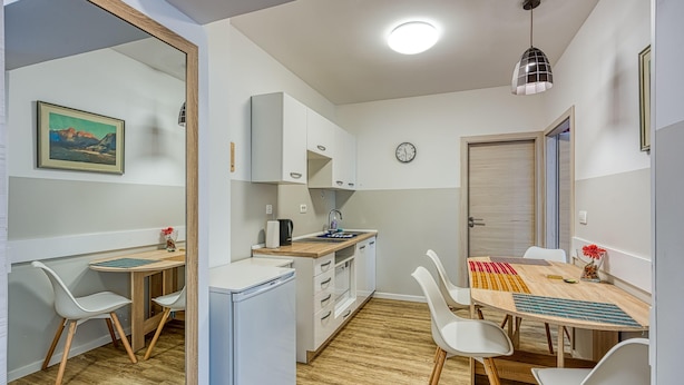 A compact kitchen with white cabinets, a wooden countertop, and a sink. There is a dining table with chairs and a clock on the wall. - Apartments Jantar - Two Bedroom n 3 (Novo Mesto)