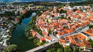 An aerial view of a town with a river, featuring a bridge, historic buildings with red roofs, and a prominent church tower. - Apartments Jantar - Two Bedroom n 3 (Novo Mesto)
