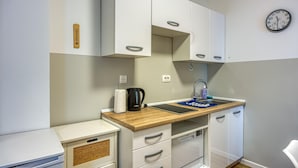 A compact kitchenette with white cabinets, a wooden countertop, a sink, and a clock on the wall. - Apartments Jantar - Two Bedroom n 3 (Novo Mesto)
