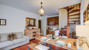 Un accogliente soggiorno con un tavolo da pranzo in legno apparecchiato per quattro persone, un divano e una scala che conduce a una cucina con armadietti in legno.