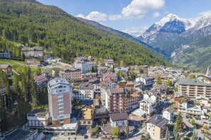 A town with a mix of modern and traditional buildings, surrounded by lush green mountains and a snow-capped peak in the background. - La Torre In The Center Of Town (Sauze d'Oulx)
