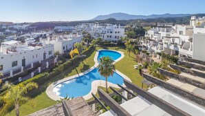 Un quartier résidentiel avec des bâtiments blancs, une piscine en forme de courbe et une montagne en arrière-plan.