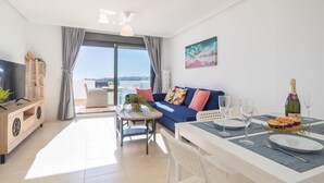 Un salon moderne avec un canapé, une table à manger pour deux personnes, un téléviseur et un balcon agrémenté de rideaux.