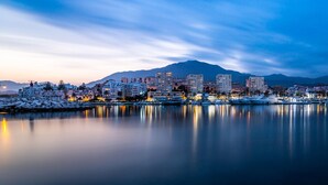 Un paysage urbain côtier au crépuscule, avec des bâtiments se reflétant sur des eaux calmes, une montagne en arrière-plan et un sol recouvert de neige.