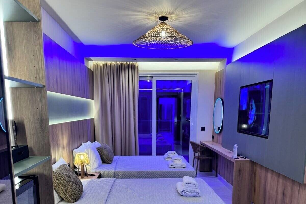 Una habitación de hotel moderna con dos camas, un escritorio, un televisor y un baño con puerta de vidrio.