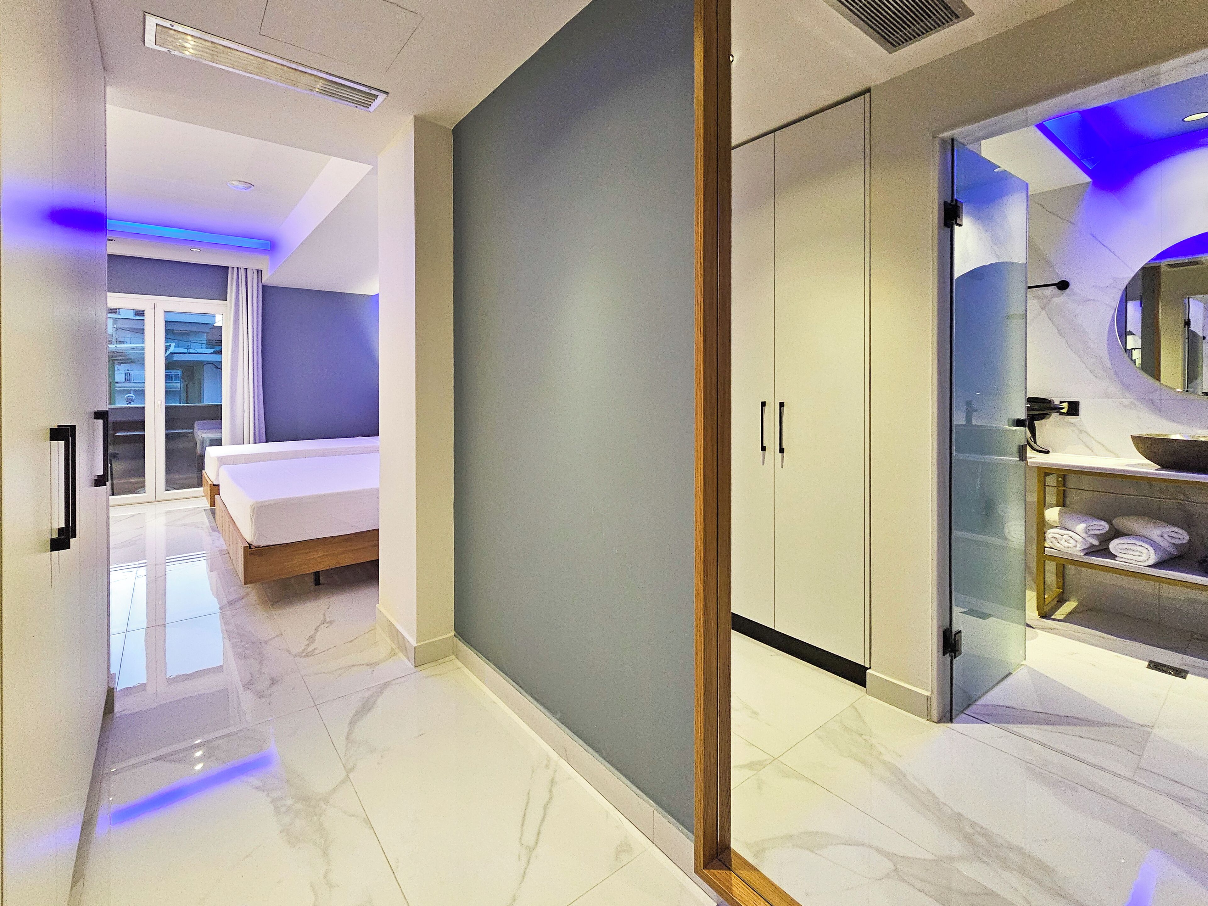 A modern hotel room with a bed, a wardrobe, and a bathroom with a sink and mirror.