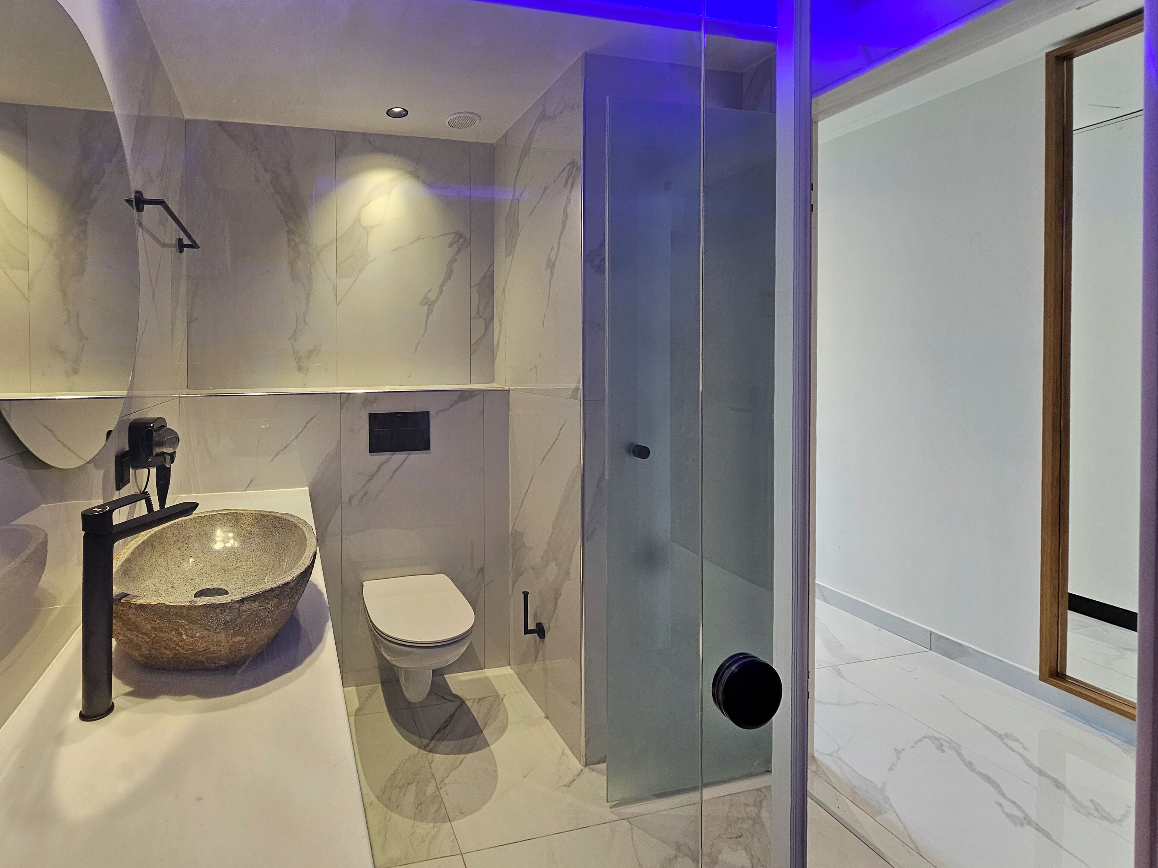 A modern bathroom with a stone sink, toilet, and glass shower enclosure.