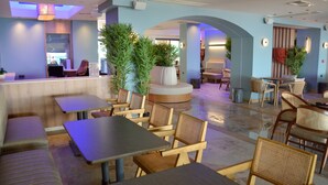 Un restaurante moderno con mesas y sillas de madera, un área de asientos central y plantas en macetas.