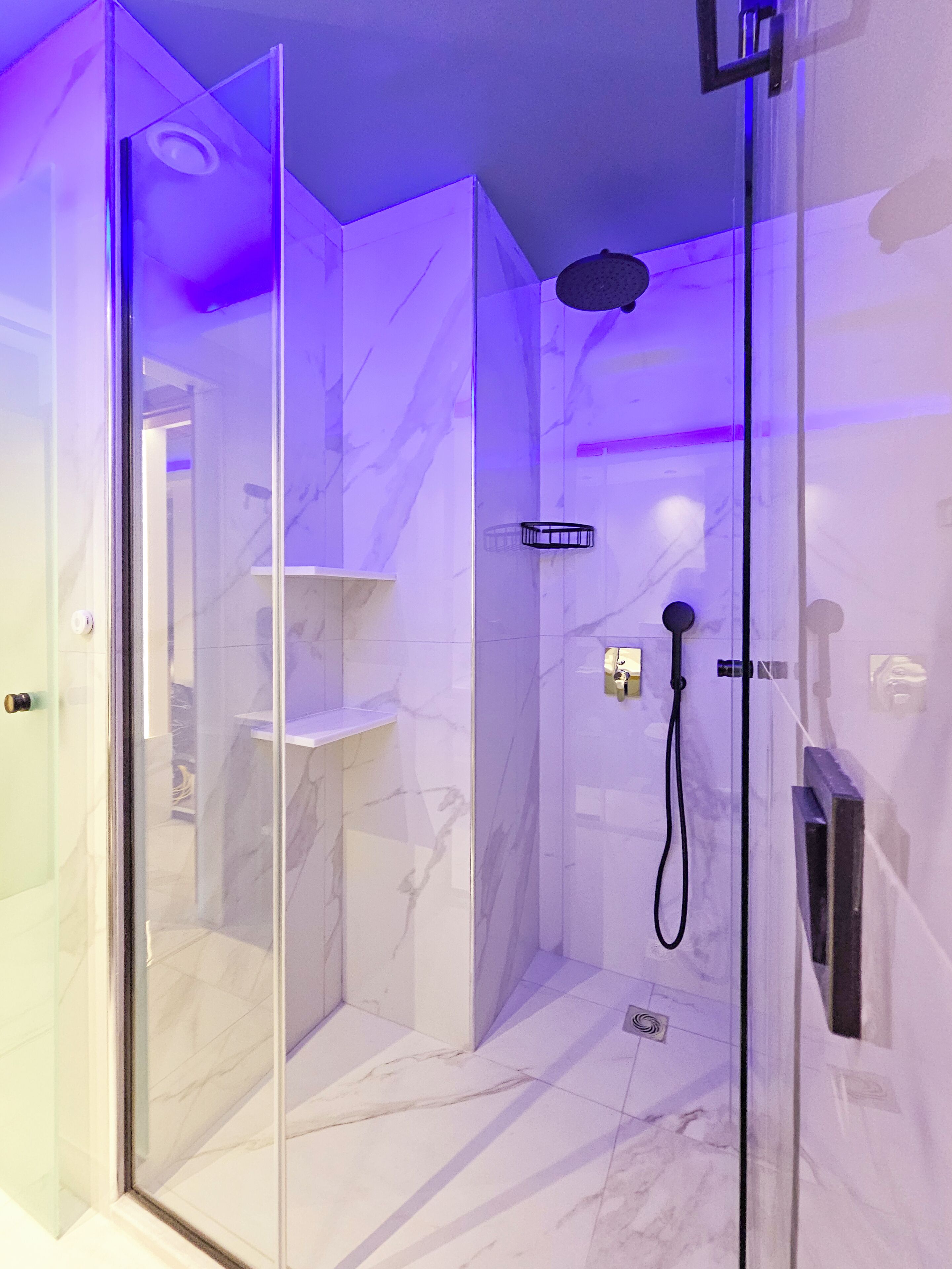 A modern shower enclosure with a glass door, marble walls, and a handheld showerhead.