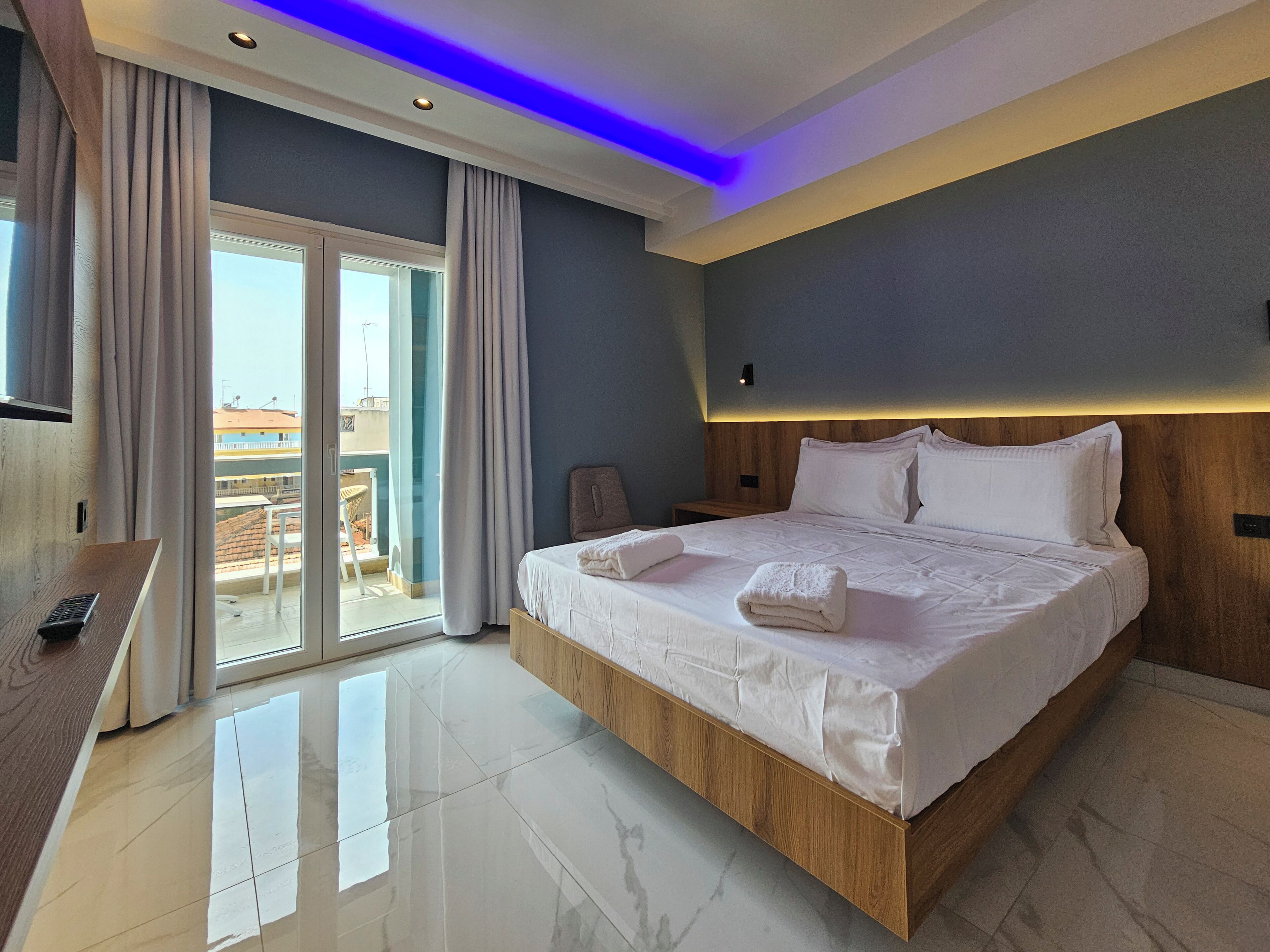 Una habitación de hotel moderna con una cama grande, un cabecero de madera, un televisor y un balcón con vistas.