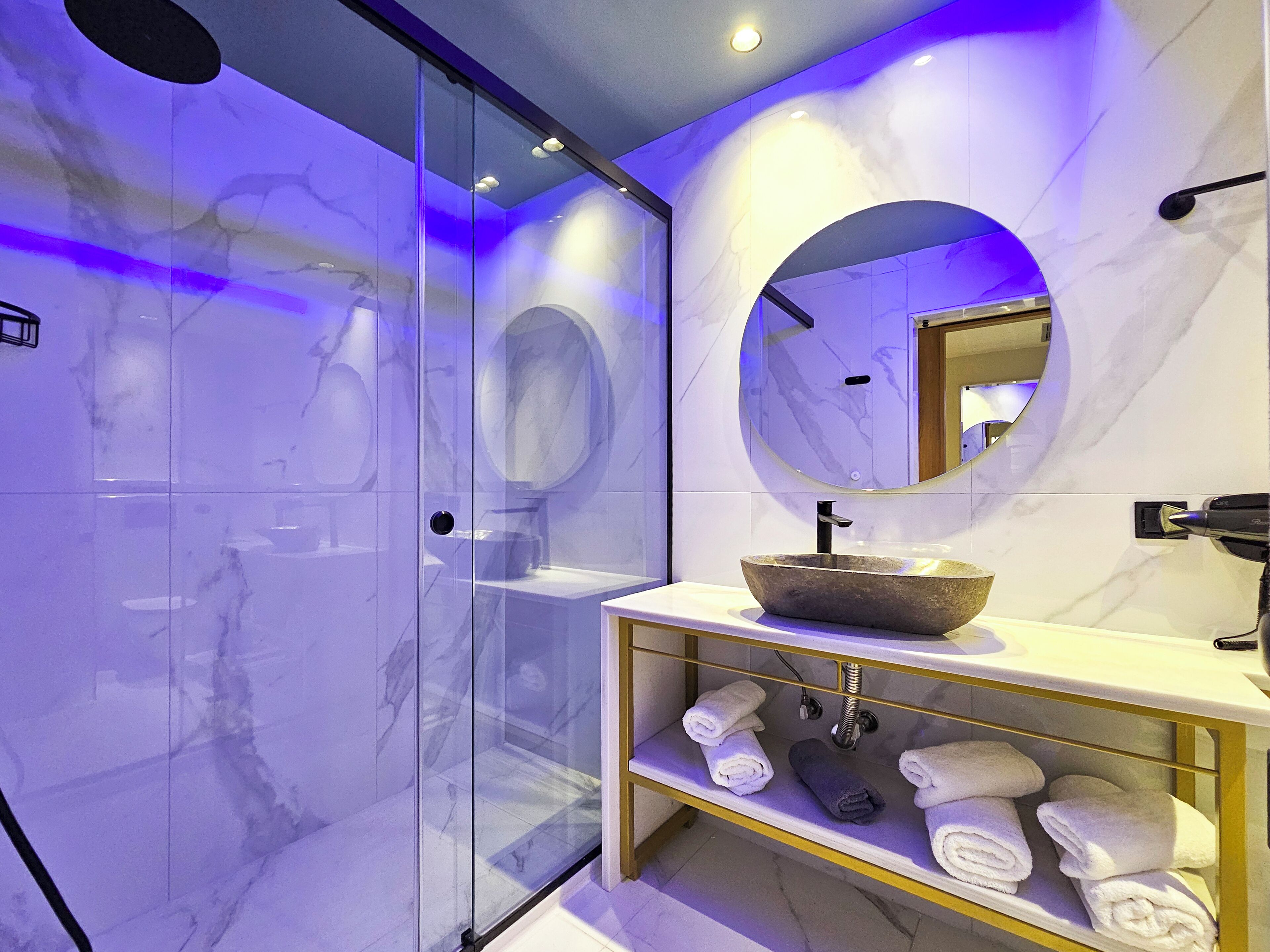 A modern bathroom with a glass-enclosed shower, a marble vanity with a bowl sink, and a mirror with a circular frame.