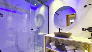 A modern bathroom with a glass-enclosed shower, a marble vanity with a bowl sink, and a mirror with a circular frame.