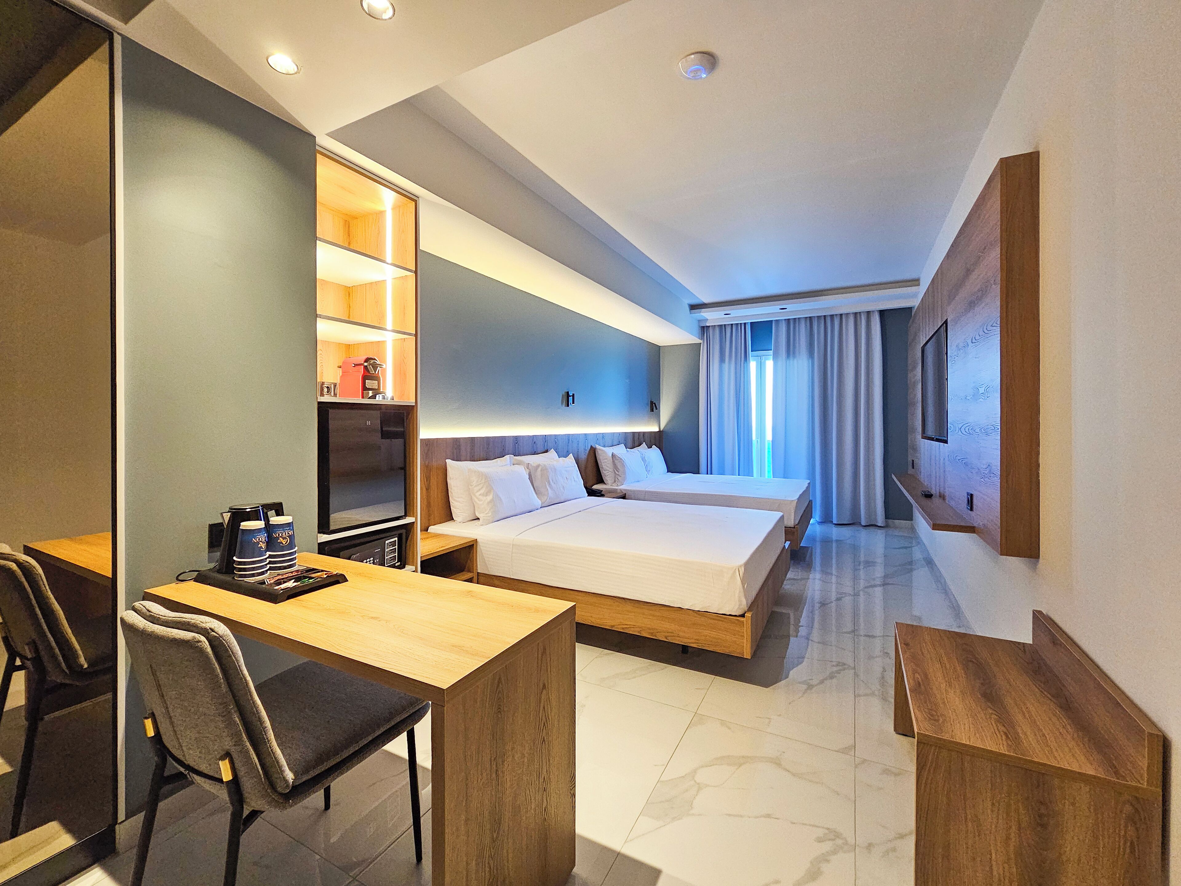 A modern hotel room with a bed, a desk, a TV, and a minibar.