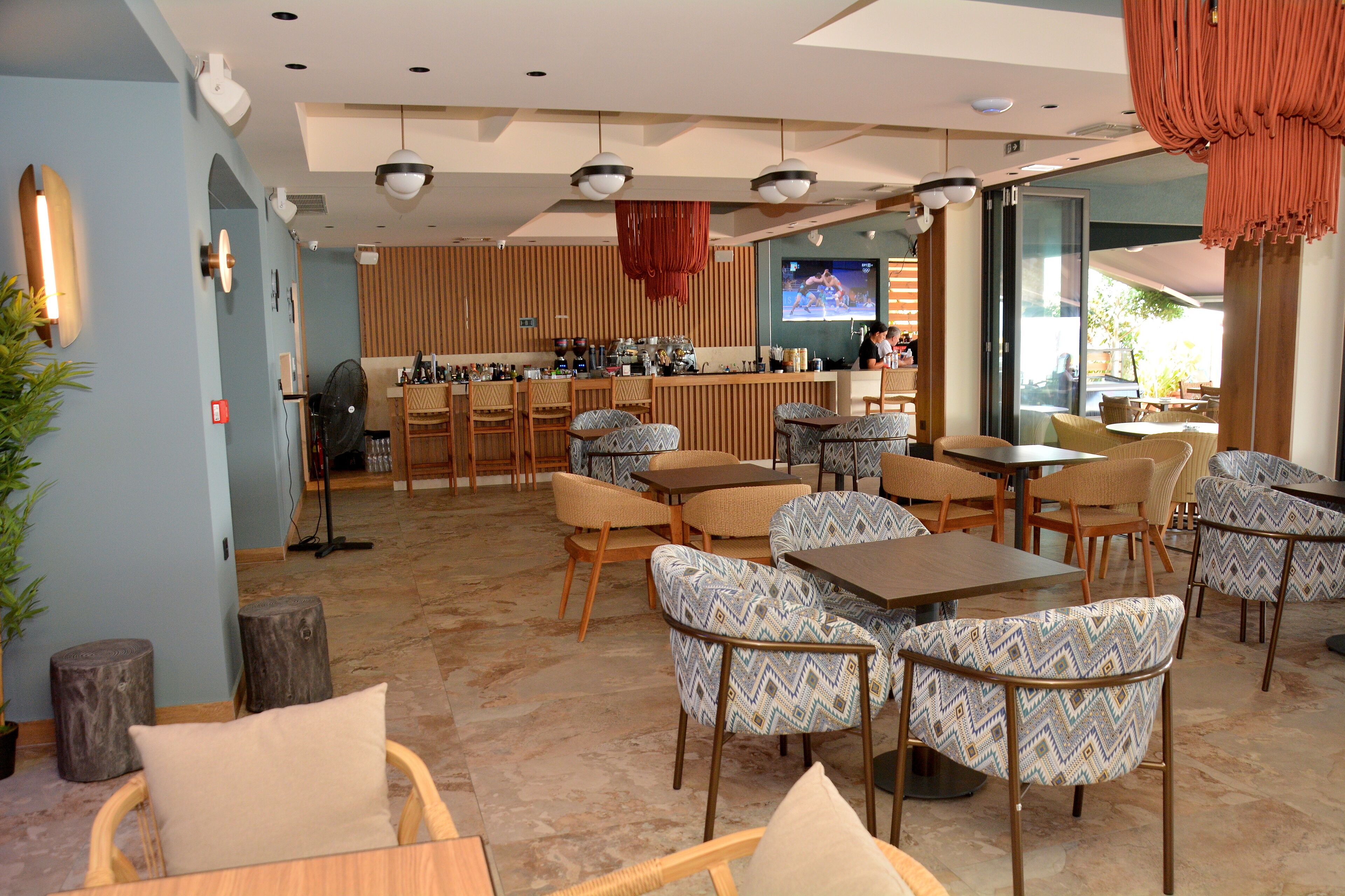 Zona de bar moderna con asientos, un televisor y una cocina al fondo.