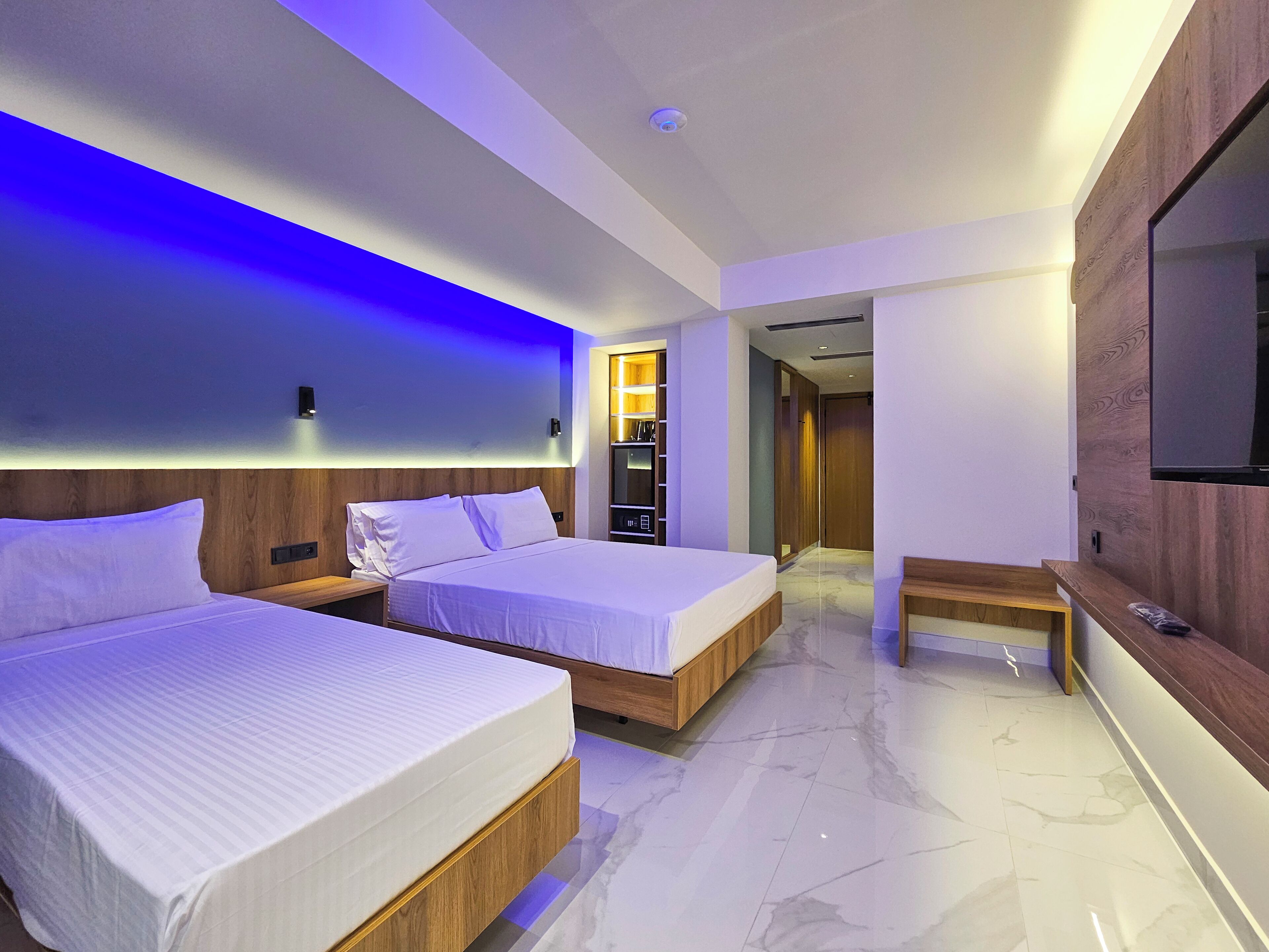 Habitación de hotel moderna con dos camas, un televisor y un banco de madera.