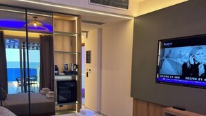 Habitación de hotel moderna con una cama grande, televisión y vista al mar a través de una puerta corredera.