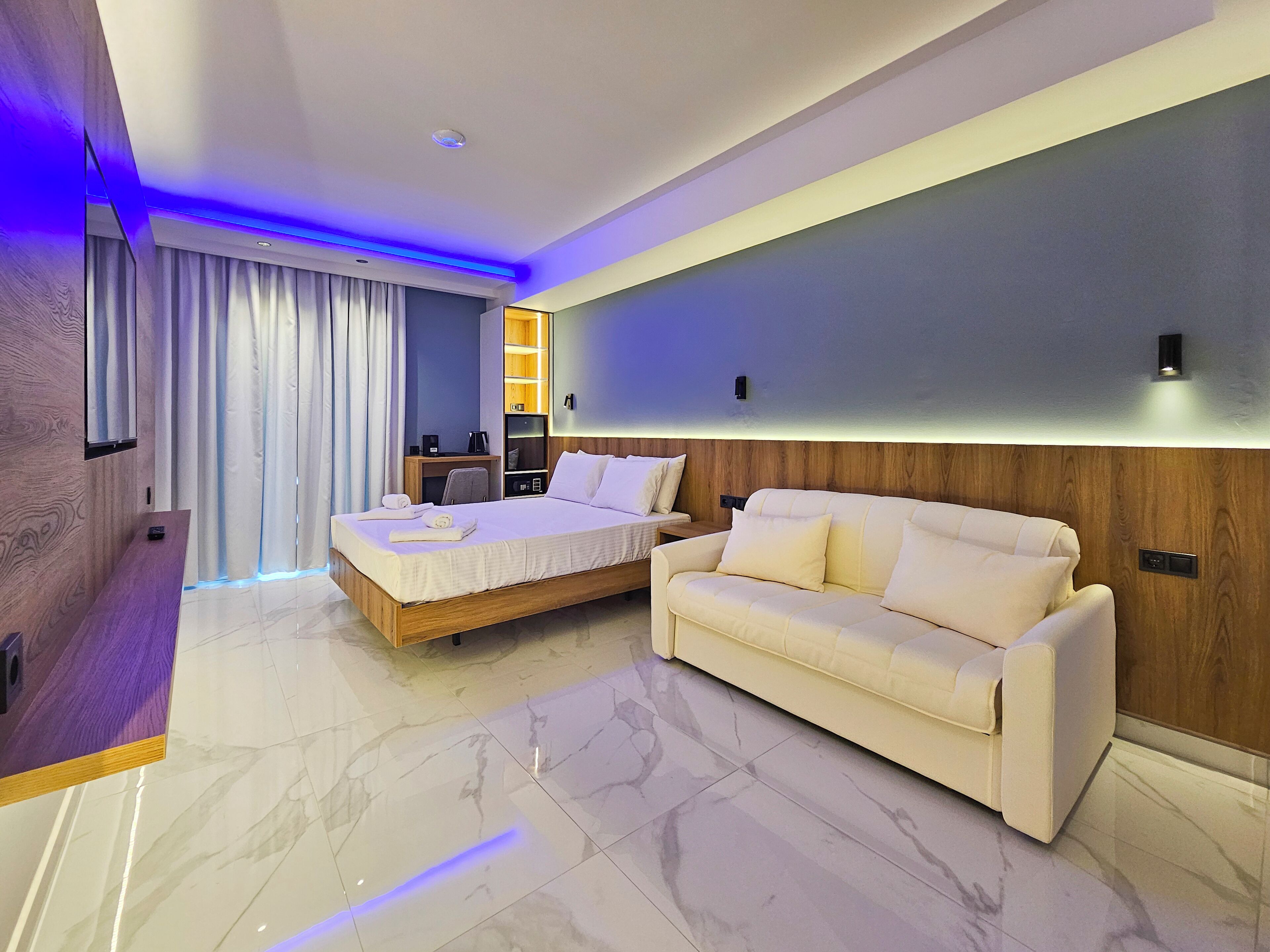 A modern hotel room with a bed, a sofa, a desk, and a bathroom area.