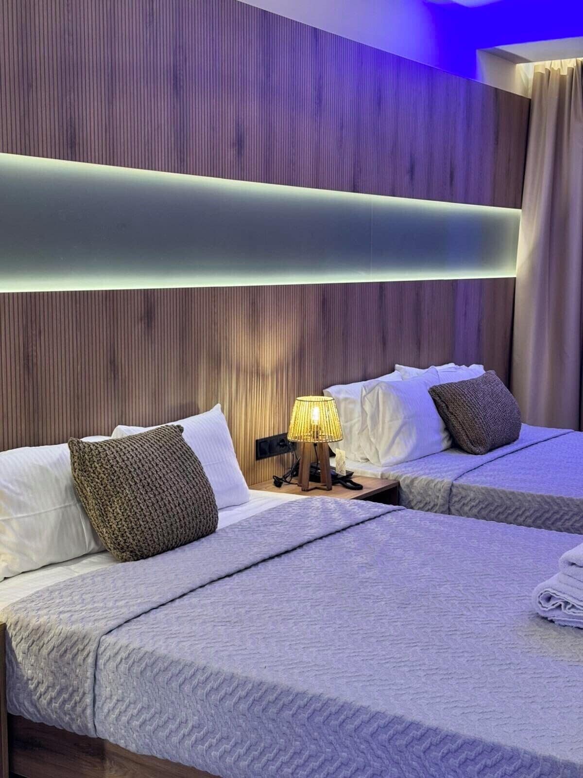 A hotel room with two beds, a wooden headboard, a bedside lamp, and a window with curtains.
