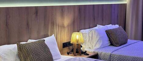 A hotel room with two beds, a wooden headboard, a bedside lamp, and a window with curtains.