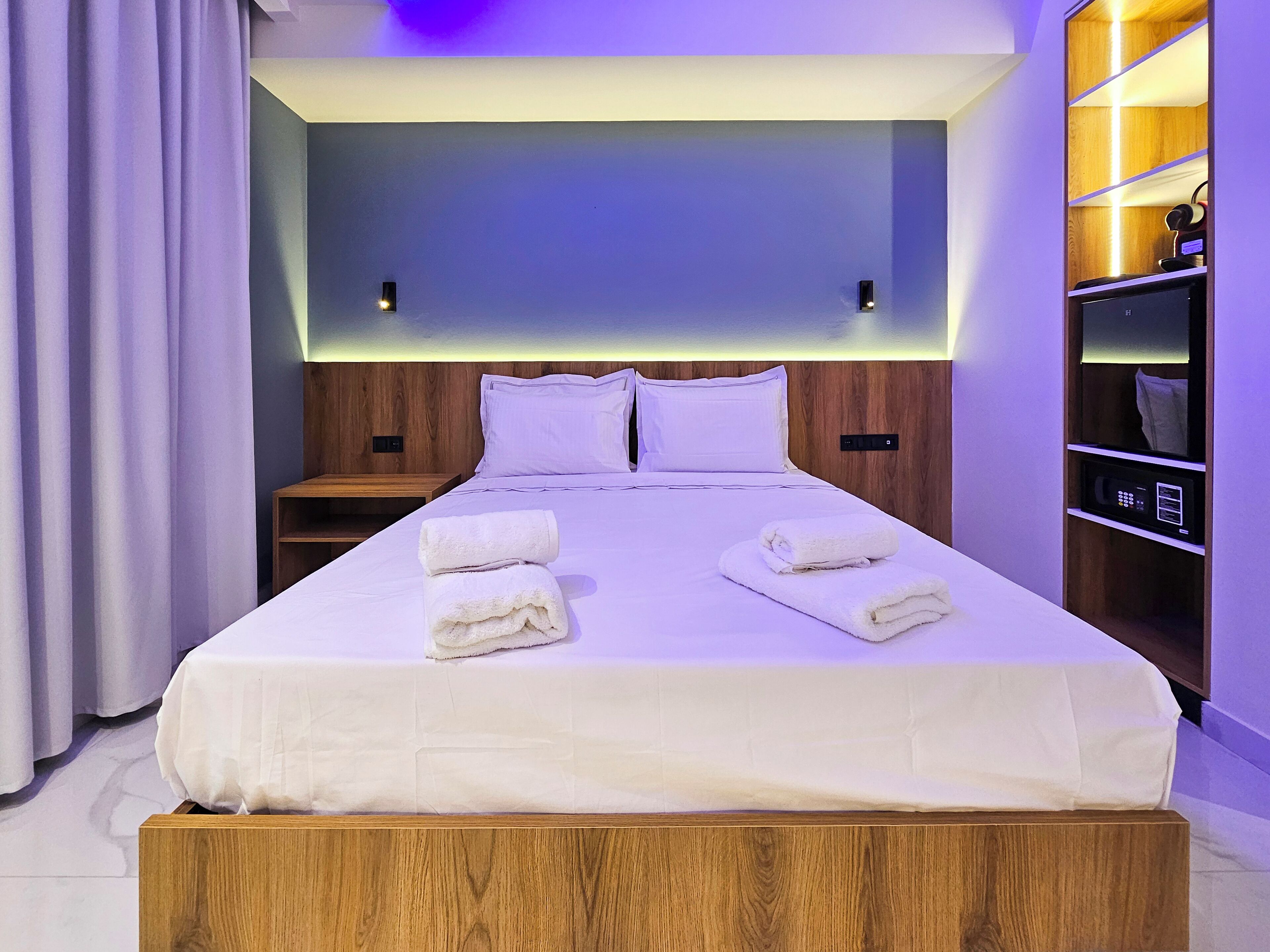 A neatly made bed with two folded towels, a wooden headboard, and a bedside table with a lamp.