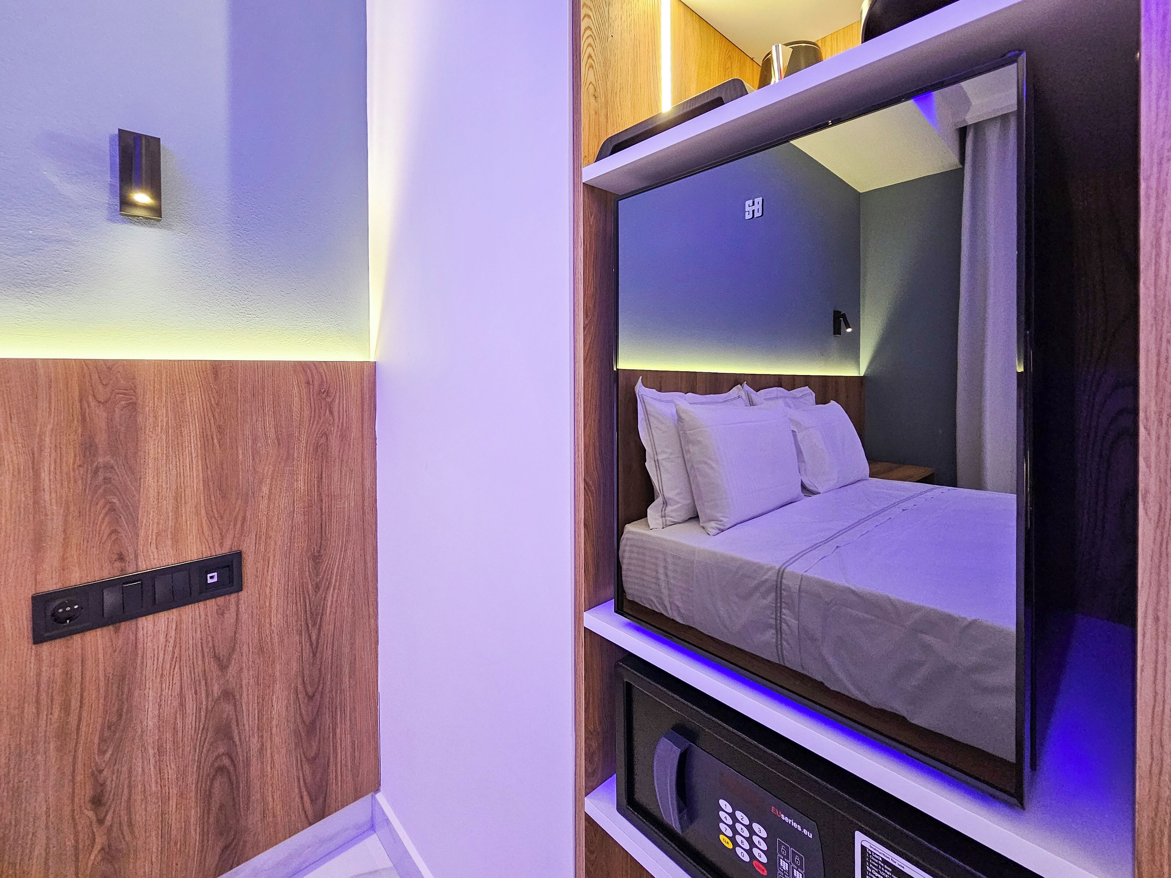 Une chambre d’hôtel moderne équipée d’un lit, d’un panneau de commande et d’une lampe fixée au mur.