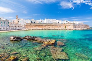 A coastal town with white buildings, clear turquoise waters, and a large rock formation in the foreground.